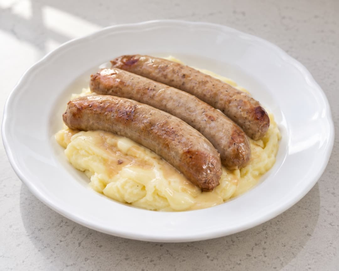 Three grilled sausages on creamy cheesy mashed potato with melted cheese sauce